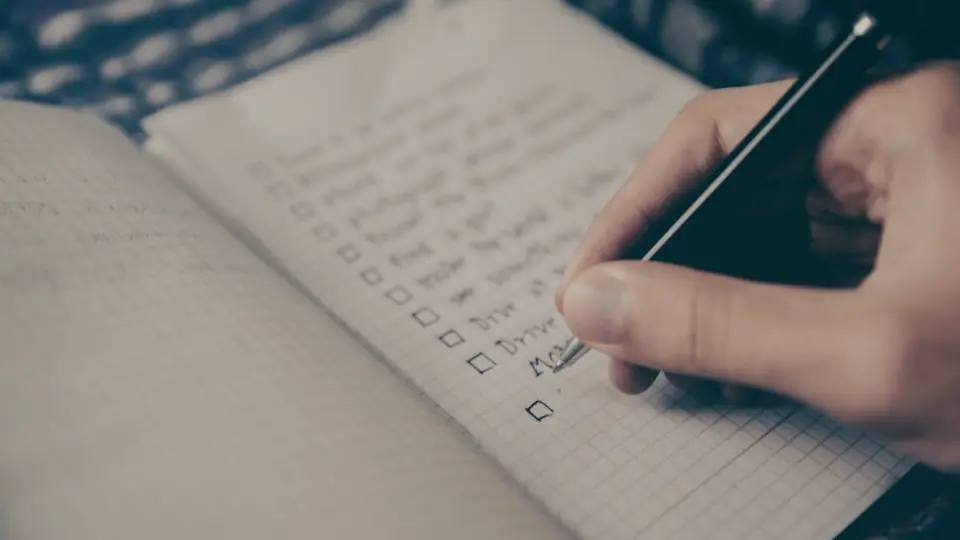 Mano escribiendo una lista de tareas en un cuaderno para decidir qué automatizar